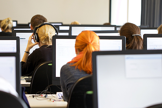 Viele Personen in einem Computerraum lösen digitale Testaufgaben vor einem Bildschirm.