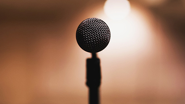 Ein Mikrofon auf einer Bühne aus Sicht der sprechenden Person im Scheinwerferlicht.