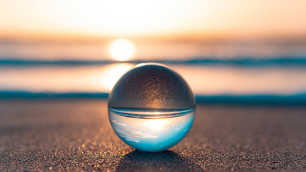 Glaskugel spiegelt den Blick auf das Meer und den Horizont bei Sonnenuntergang.